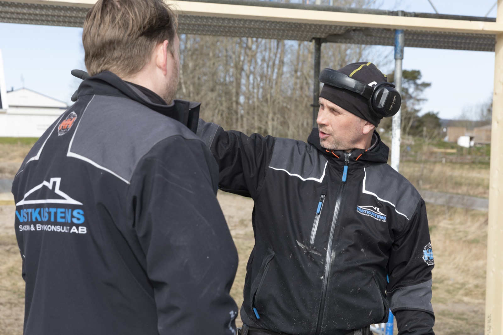 Snickare i samtal på byggplats med firmalogotyp